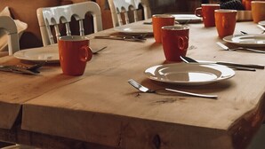 Une table de salle à manger en bois, mise avec des assiettes, des couverts et des tasses rouges.