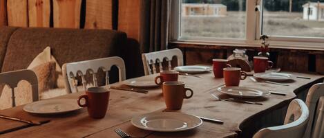 A wooden dining table set with plates, cups, and cutlery, with chairs featuring a unique design.