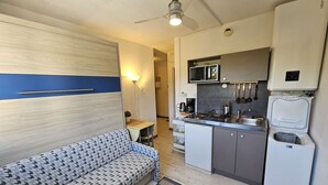Un espacio habitable pequeño con kitchenette, un sofá y un ventilador de techo.