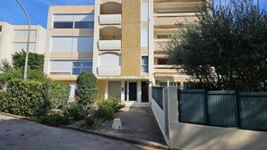 Un edificio residencial de varios pisos con entrada central, balcones y un camino de acceso con portón.