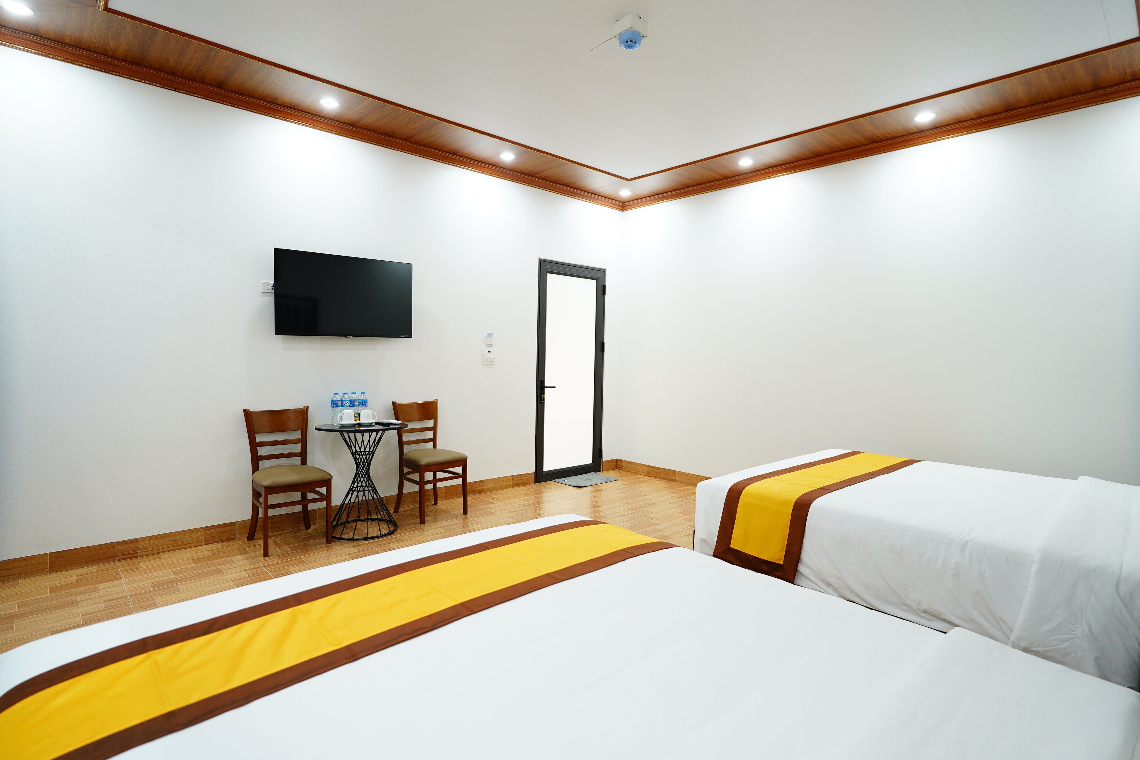A hotel room with two beds, a TV mounted on the wall, a desk with chairs, and a door.