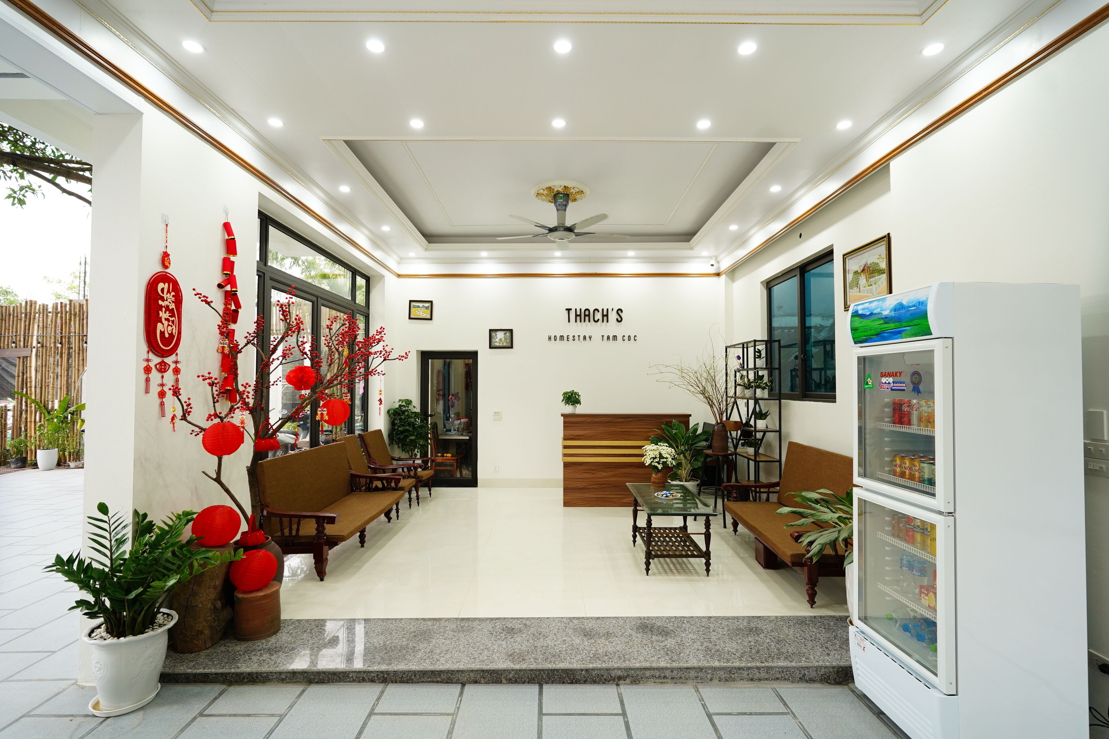A hotel lobby with seating, a refrigerator, and a sign reading "THACH'S HOMESTAY TAM COC".