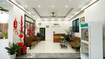 A hotel lobby with seating, a refrigerator, and a sign reading "THACH'S HOMESTAY TAM COC".