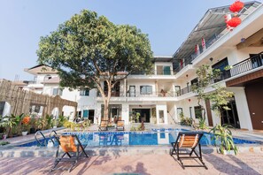 A multi-story building with a swimming pool, outdoor seating, and a large tree in the center. - Thach's Homestay Tam Coc (Hoa Lu)