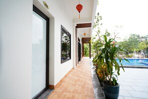 A corridor with a wooden floor, glass doors, and potted plants. - Thach's Homestay Tam Coc (Hoa Lu)