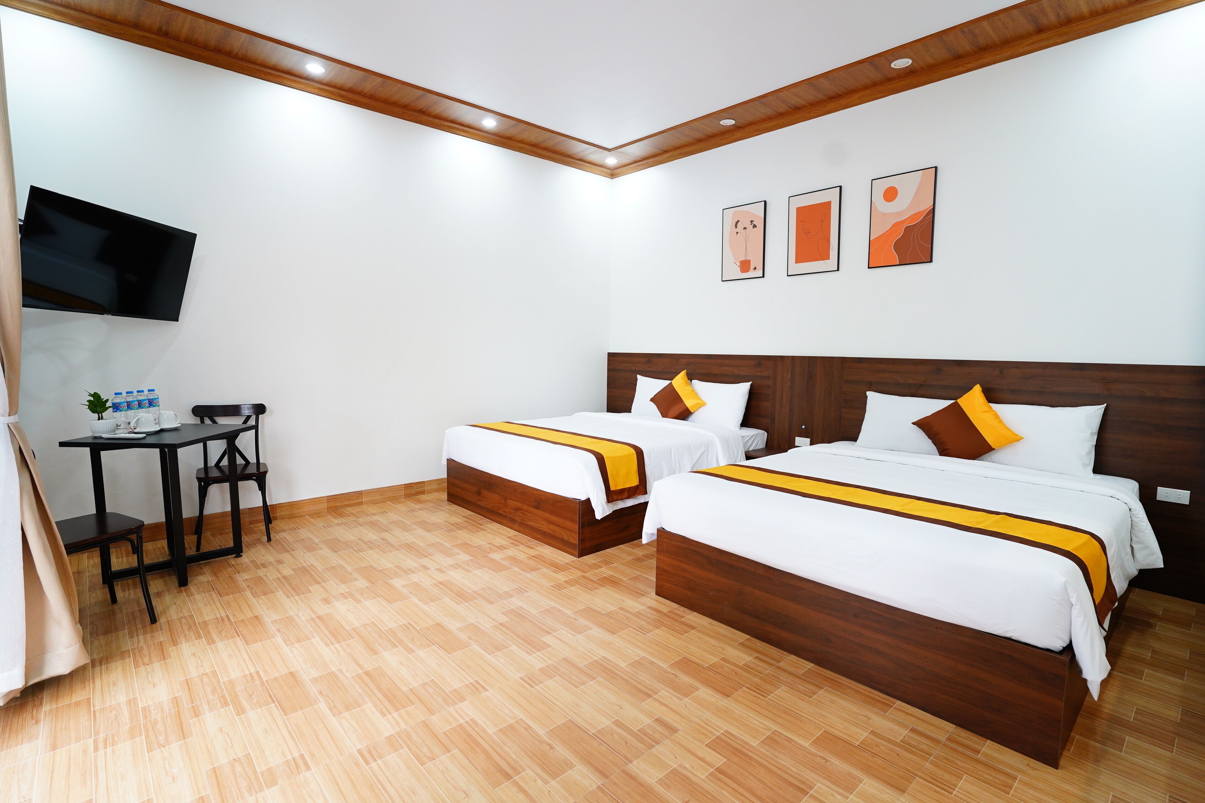A hotel room with two beds, a desk, a chair, a TV, and artwork on the wall.