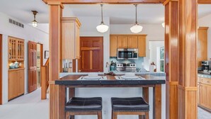 Une cuisine avec des meubles de rangement en bois, un îlot central doté de tabourets, un four à micro-ondes et une cuisinière.