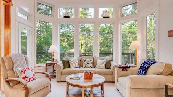 A cozy living room with a large window, a sofa, two armchairs, a coffee table, and a side table with a lamp.