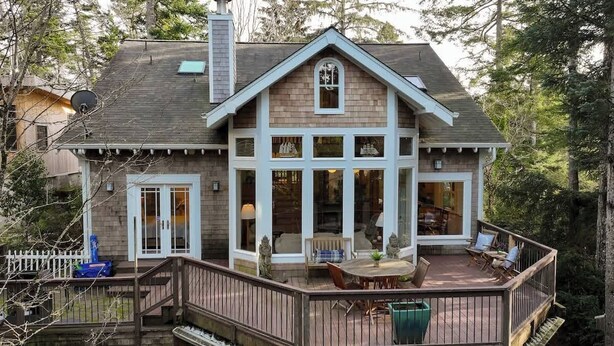 Une maison à deux étages dotée d’une terrasse, de grandes fenêtres et d’une cheminée.