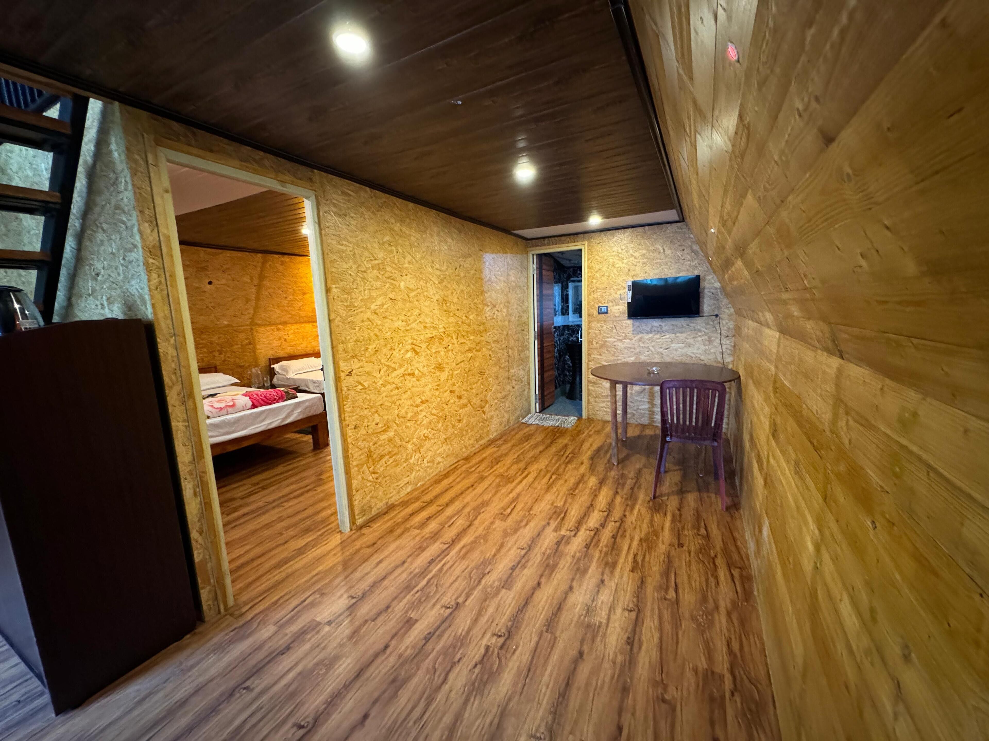 A compact room with a bed, a small table, and a television mounted on the wall.