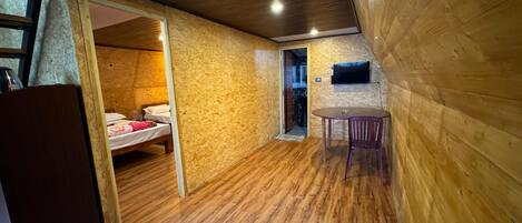 A compact room with a bed, a small table, and a television mounted on the wall.