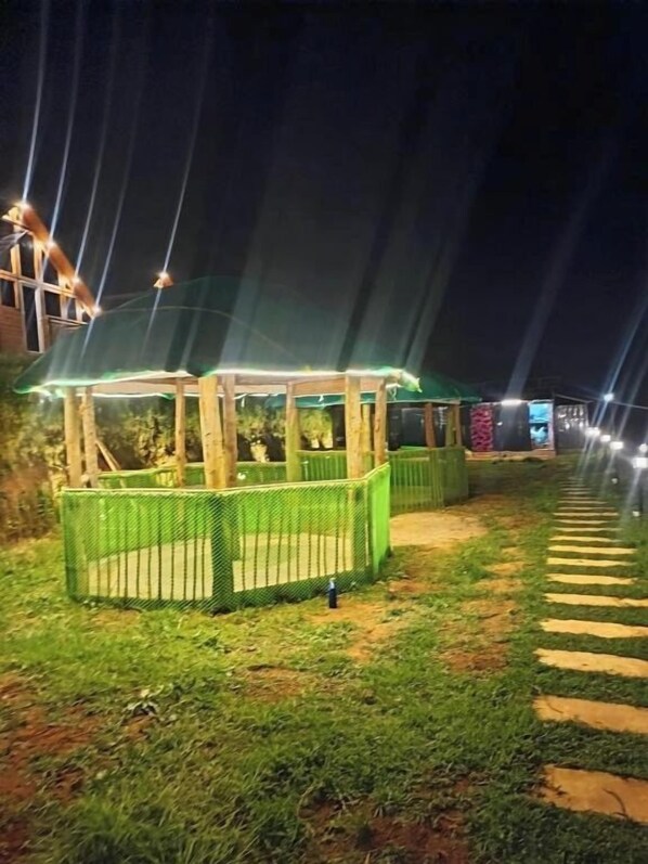 Un espacio exterior nocturno con una zona de estar techada y un sendero.