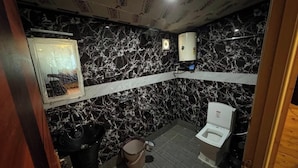 A small bathroom with a black and white marble wall, a sink, a toilet, and a trash bin. - Fairyland Resort (Kodaikanal)