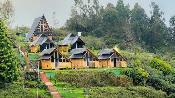 A cluster of wooden cabins with pitched roofs, surrounded by lush greenery and a hilly landscape. - Fairyland Resort (Kodaikanal)