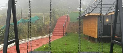 A swing set in a park with a red pathway and a wooden structure in the background.