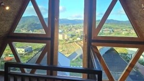 A room with a triangular window design, offering a view of a landscape with buildings and hills. - Fairyland Resort (Kodaikanal)