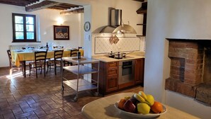 A kitchen with a brick fireplace, a dining area with a table set for four, and a fruit bowl on the counter. - Villa sleeps 14 with private pool (Monteroni d'Arbia)