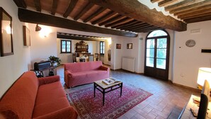 A cozy living room with a red sofa, a coffee table, and a bookshelf. - Villa sleeps 14 with private pool (Monteroni d'Arbia)