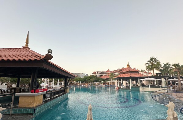 A large swimming pool with a statue in the center, surrounded by lounge chairs and umbrellas.