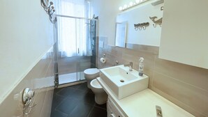 A modern bathroom with a glass shower enclosure, a toilet, a sink with a mirror above, and a handheld showerhead. - Casa Elia - Procchio - Casa Elia - Procchio (Marciana)
