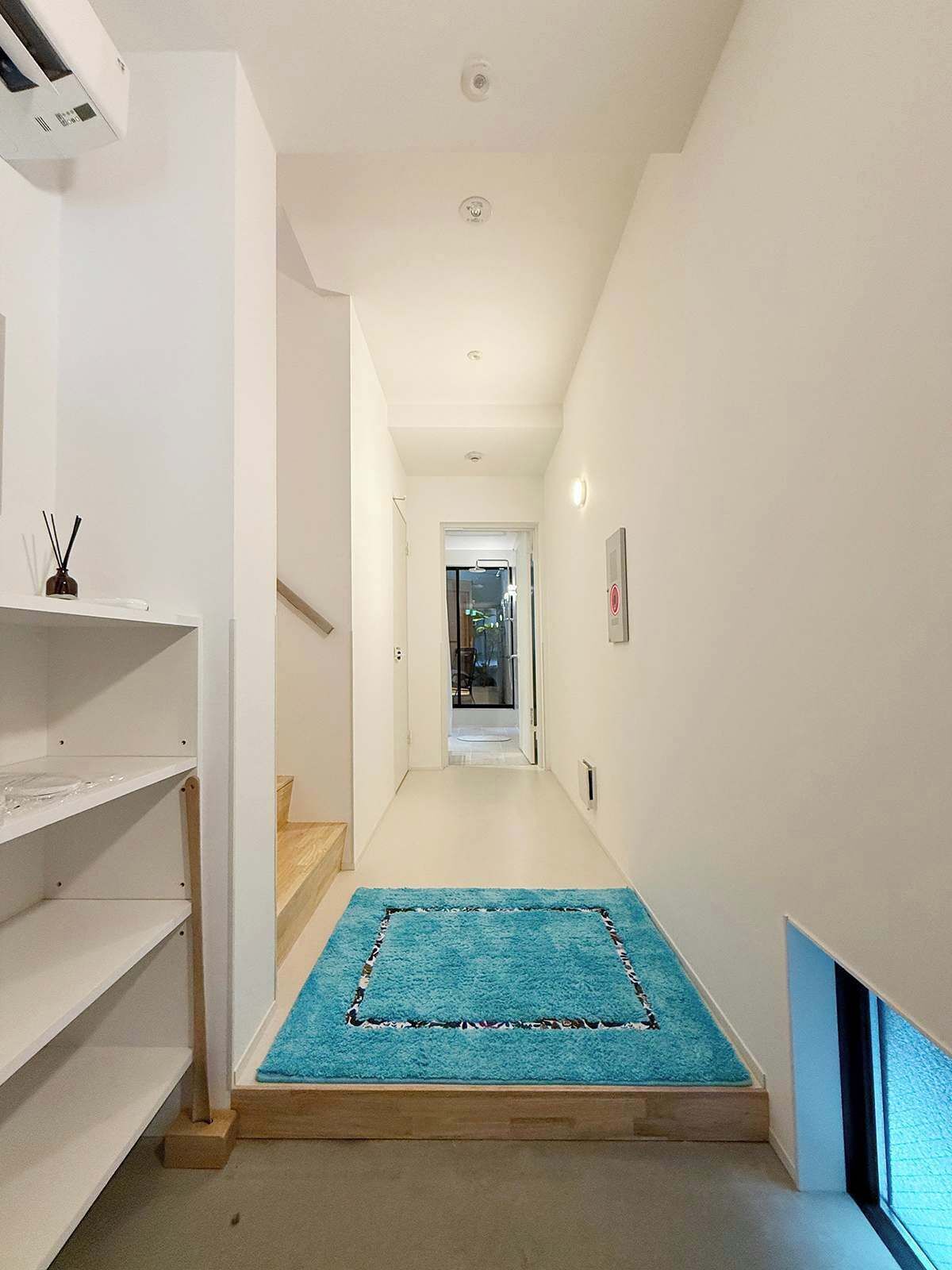 A narrow hallway with a blue carpet leading to a door. There are white walls and a white ceiling with recessed lighting.