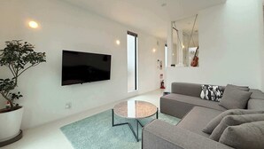 Una sala de estar moderna con un televisor de pantalla plana, un sofá gris, una mesita redonda pequeña y una planta en maceta.