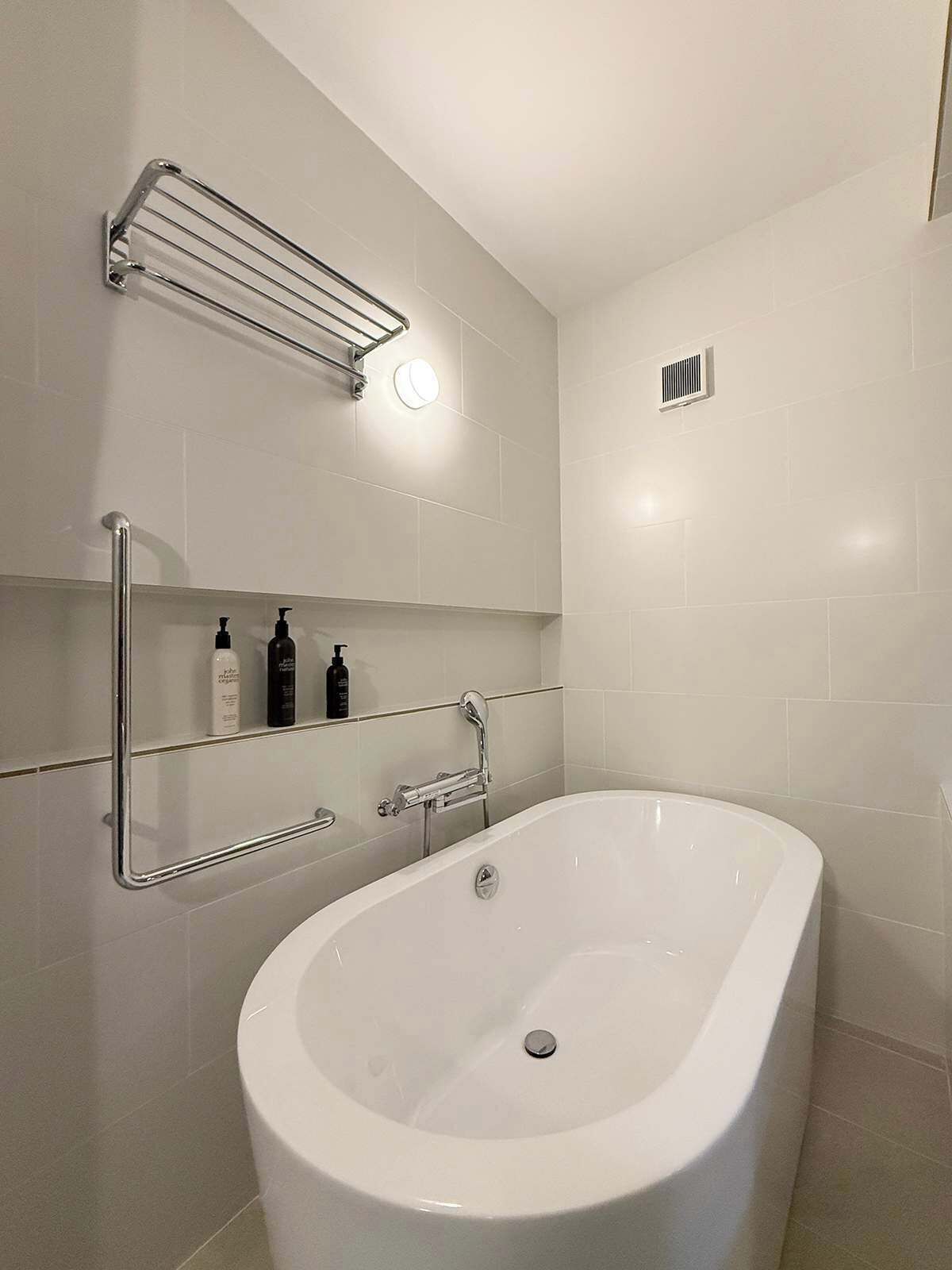 A modern bathroom with a freestanding bathtub, chrome towel racks, and a wall-mounted shelf with toiletries.