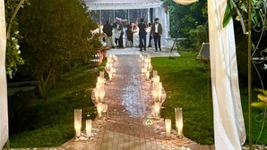Une allée pour une cérémonie de mariage en plein air, décorée de draperies blanches, de bougies et bordée d’invités.