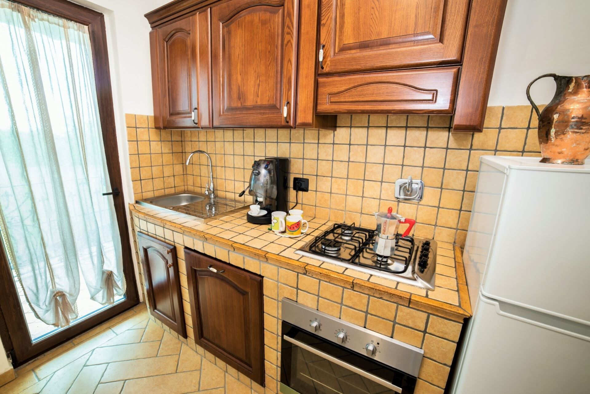A kitchen with wooden cabinets, a tiled backsplash, a gas stove, a sink, and a refrigerator.