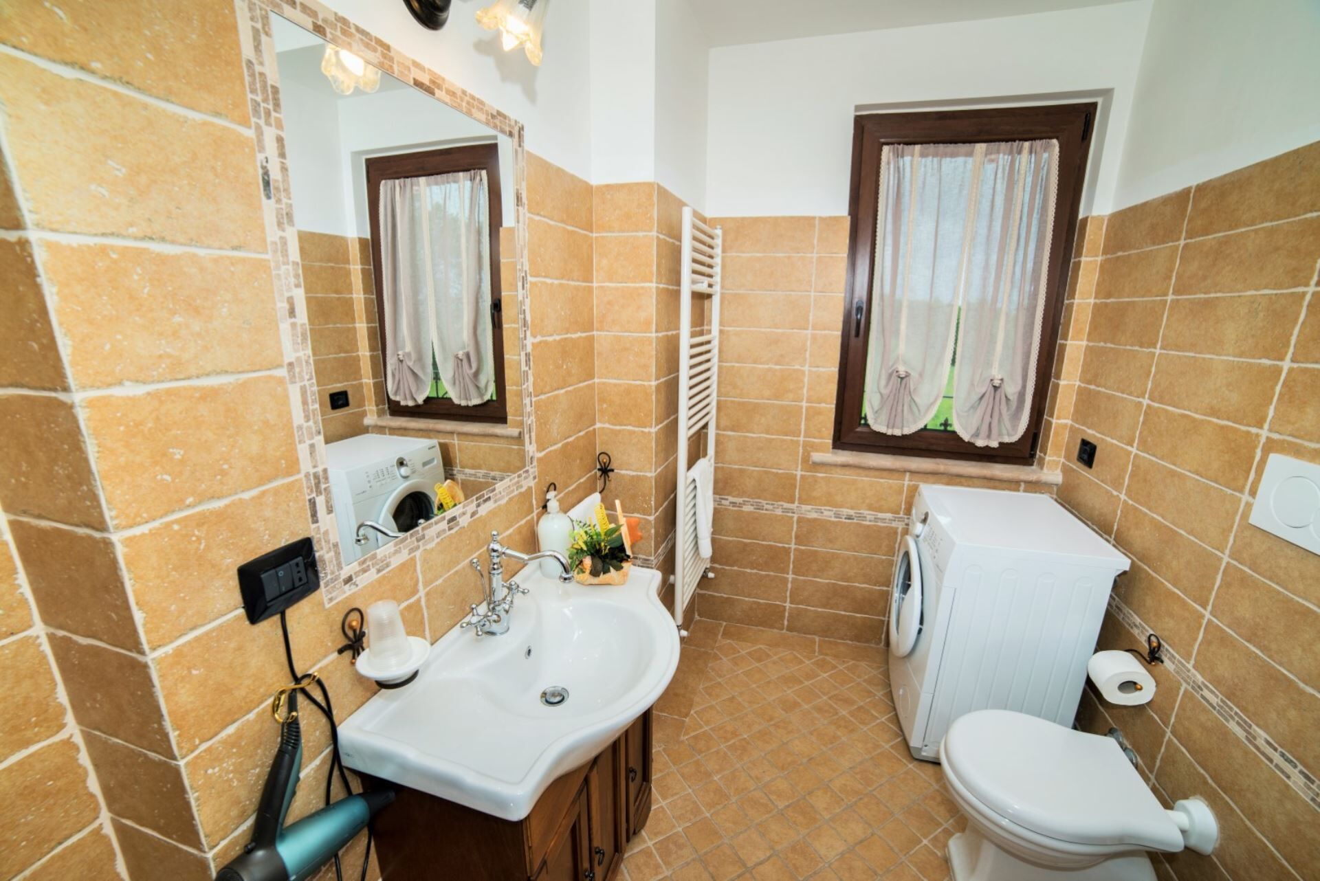 A bathroom with a sink, mirror, toilet, and a window with curtains.