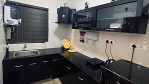 A compact kitchen with black countertops, a built-in oven, a washing machine, and a window with blinds. - S ELLA Residency (Kotagiri)
