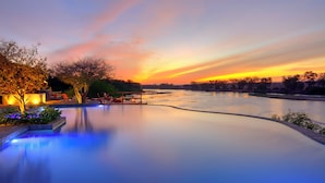 A serene riverside pool area with a sunset view, surrounded by trees and outdoor seating. - Kudu Safari Camp (Tsavo East)