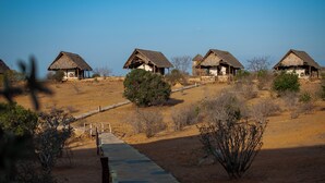 A row of thatched-roof huts with stone pathways and sparse vegetation. - Kudu Safari Camp (Tsavo East)