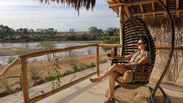 A person sitting in a wicker chair on a balcony overlooking a river and landscape.
