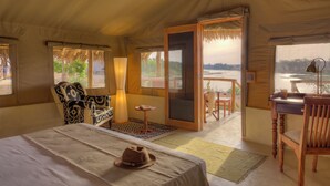 A room with a bed, a chair, a desk, and a view of a body of water. - Kudu Safari Camp (Tsavo East)