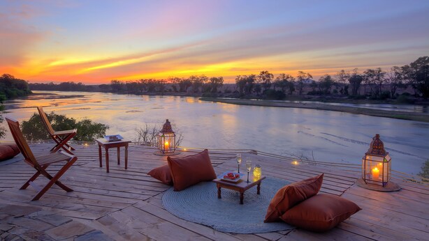 A sunset view from a deck with wooden chairs, a table with a candle, and lanterns. - Kudu Safari Camp (Tsavo East)