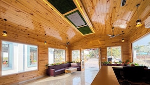 A spacious room with wooden ceiling and walls, large windows, a long counter, and a seating area with a sofa and chairs. -  Wonderwood Corbett Resort (1min walk to River with Deep Jungle Trail) (Ramnagar)