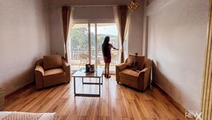 A spacious living room with wooden flooring, two leather sofas, a coffee table, and a large sliding glass door leading to an outdoor balcony. -  Wonderwood Corbett Resort (1min walk to River with Deep Jungle Trail) (Ramnagar)