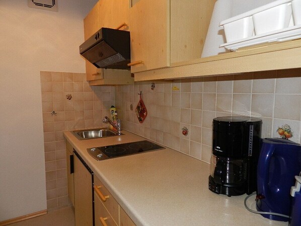 A compact kitchen with a double sink, a black coffee maker, and wooden cabinets. - Apartment (02) with balcony and extra kitchen (Reit im Winkl)