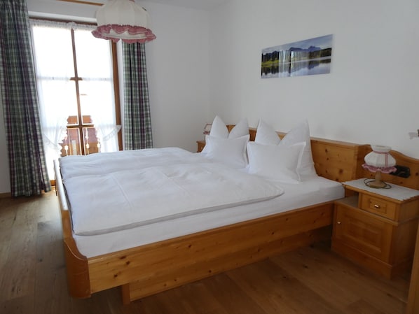 Un dormitorio con cama de madera, ropa de cama blanca, una mesita de noche, una lámpara y un cuadro en la pared.