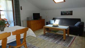 A cozy living room with a wooden ceiling, a sofa, a television, and a dining area with a table and chairs. - Apartment (03) with balcony and extra kitchen (Reit im Winkl)