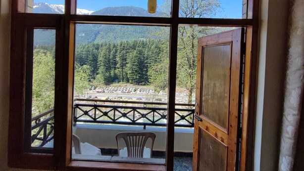 A room with a large window offering a view of a mountainous landscape and a parking area. - Chichoga Holiday Inn Manali (Manali)