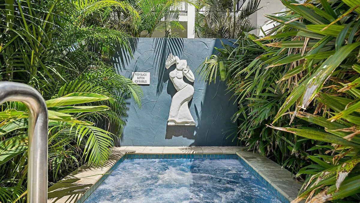A pool area with a statue, surrounded by lush greenery and a sign instructing to push a button for bubbles.