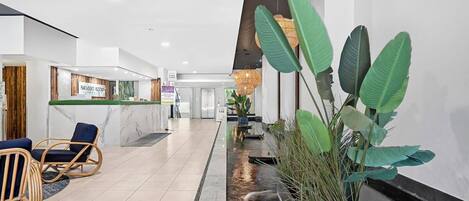 A modern reception area with a marble reception desk, wicker chairs, and a water feature.