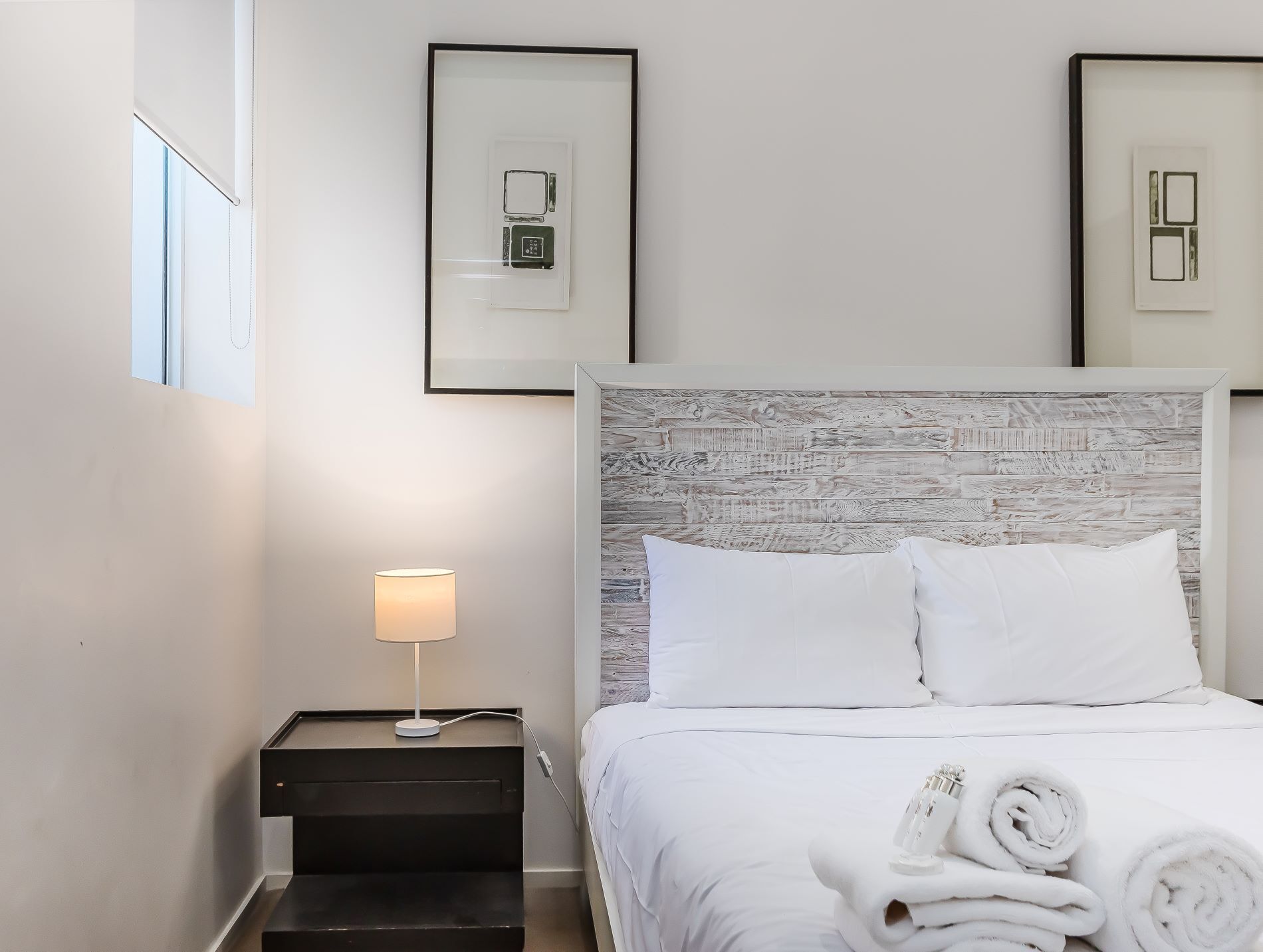 A hotel room with a bed, a nightstand with a lamp, and two framed pictures on the wall.