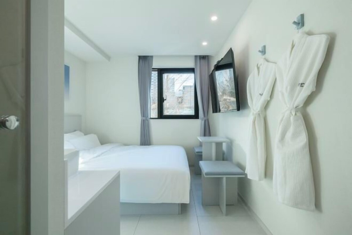 Habitació d'hotel moderna amb un llit, una petita taula de nit, una banca i un televisor fixat a la paret.