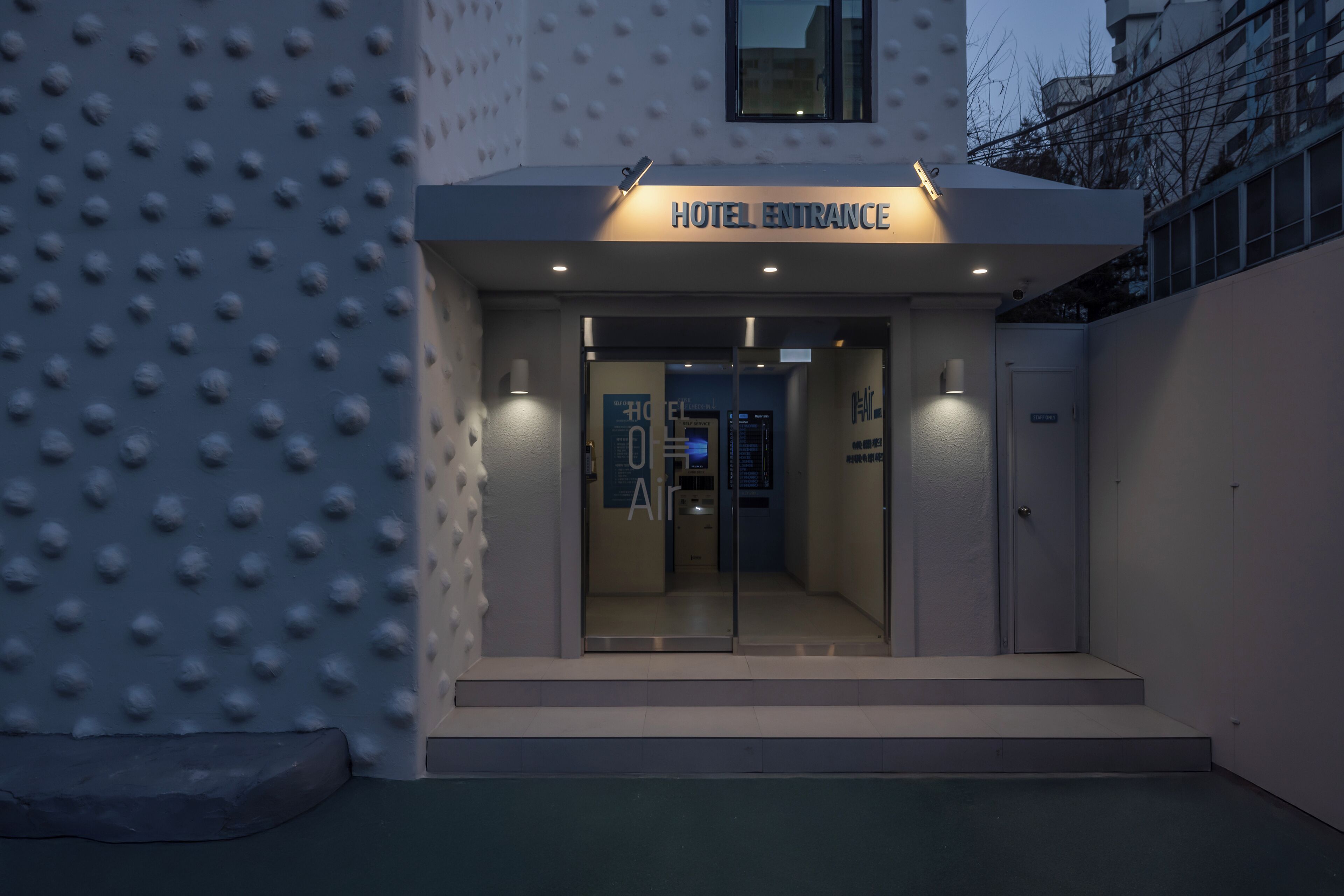 Ingresso di un hotel, con una segnaletica che riporta 'HOTEL ENTRANCE' e un display digitale sopra la porta.