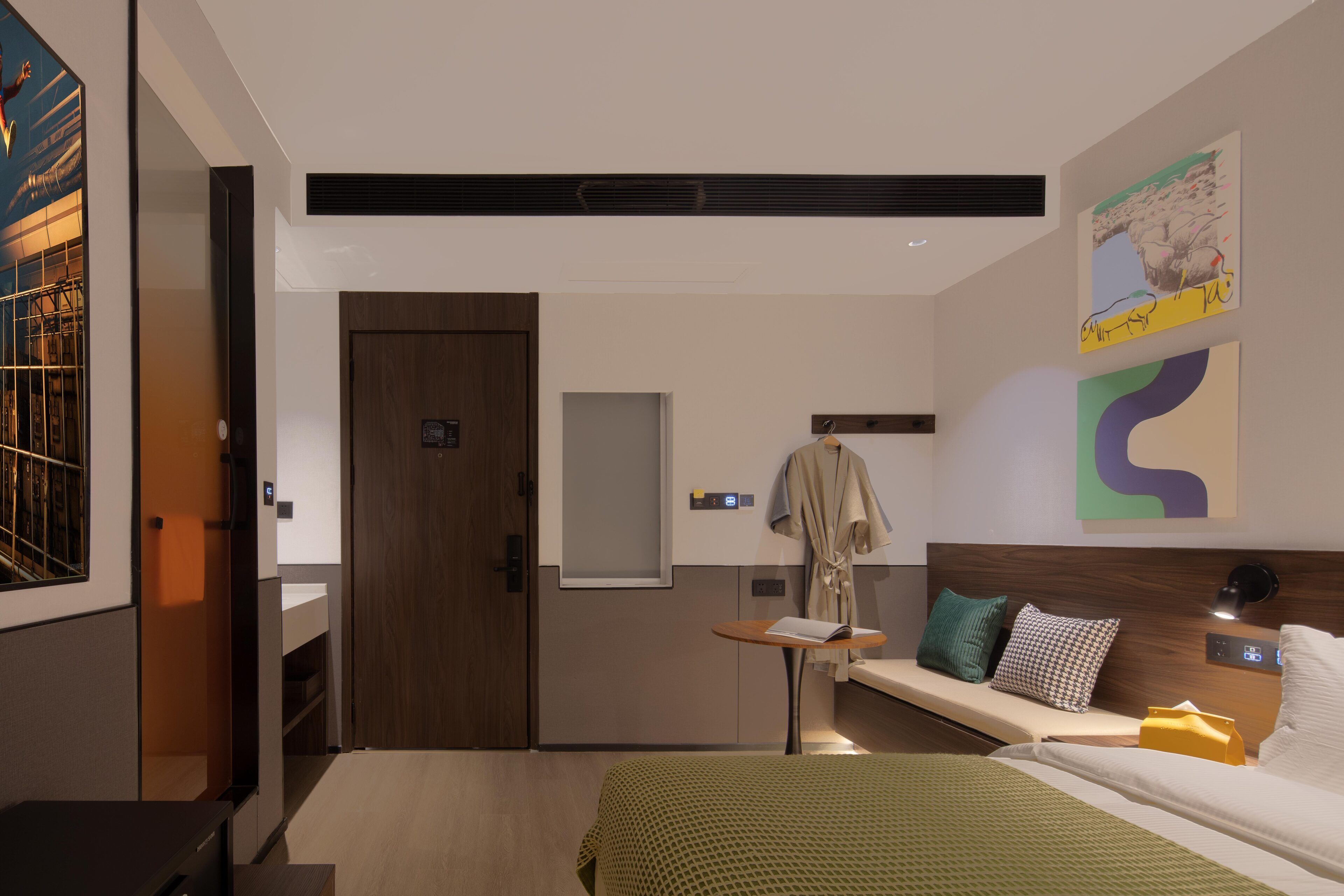 Habitación de hotel moderna con cama, mesita de noche pequeña, bata colgada y una obra de arte en la pared.
