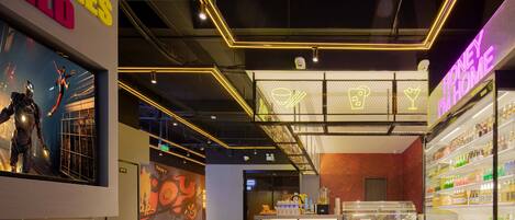 A modern interior with a neon sign reading "HONEY IN HOME," a display case with various beverages, and a large poster of a superhero.