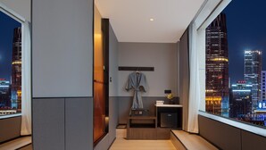 Habitación de hotel moderna con vistas a la ciudad, una bata colgada en la pared y una pequeña mesa con una lámpara.